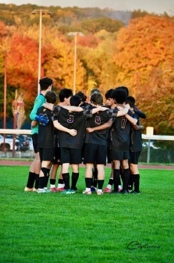 Soccer team huddled together in front of autumn trees